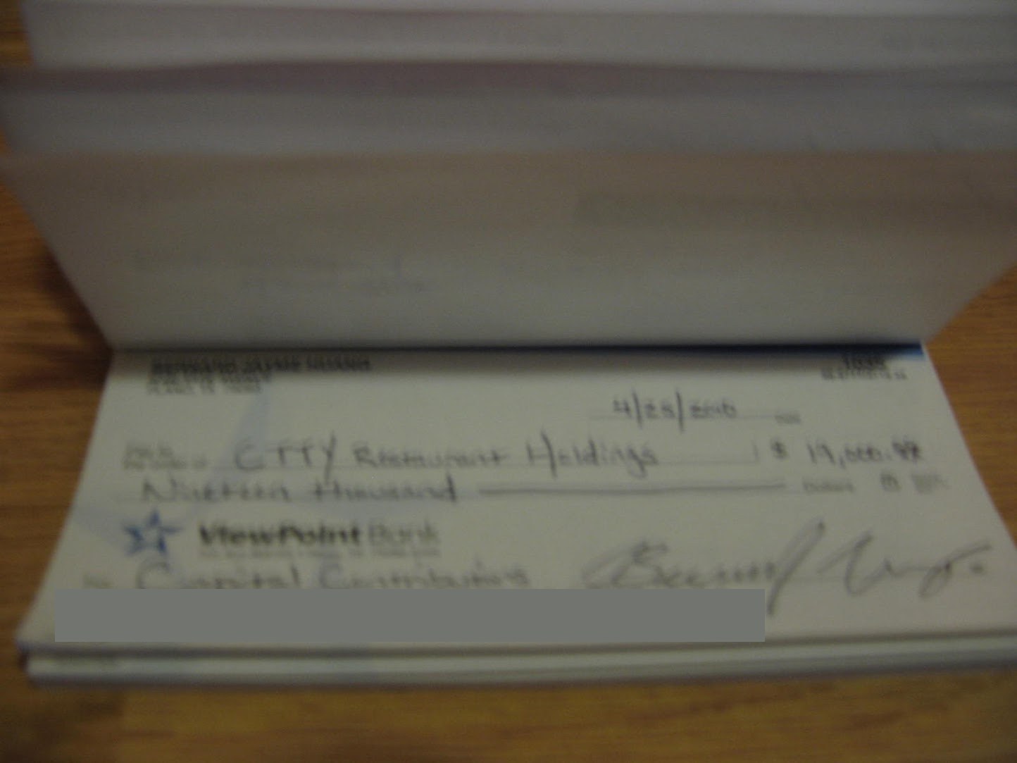 A handwritten personal check dated April 25, 2010 for $19,000 to a restaurant holdings company, memo line Capital Contributions, with the bank account numbers covered by a gray redaction bar.